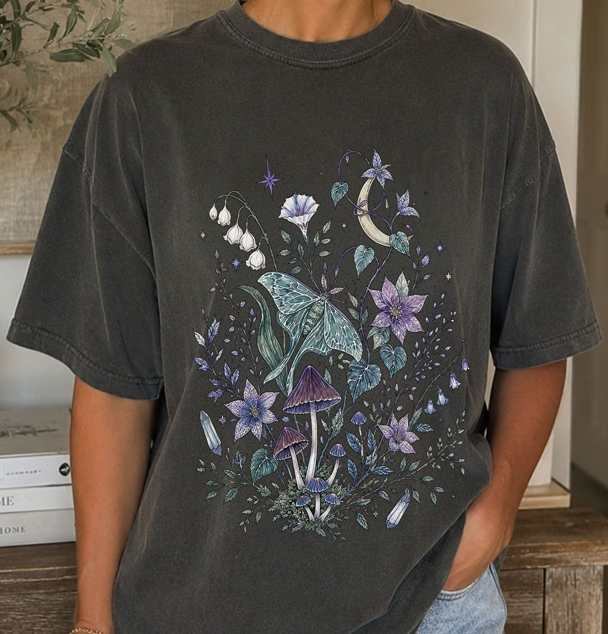 Person wearing a dark gray t-shirt with a nature-themed design featuring mushrooms and flowers.